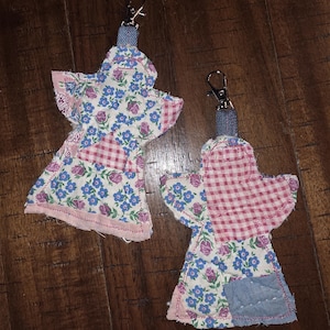 May include: Two fabric angel ornaments featuring patchwork designs with blue floral, pink rose, and red gingham patterns. Each angel has a denim fabric loop at the top attached to a silver-toned metal lobster clasp for hanging purposes.
