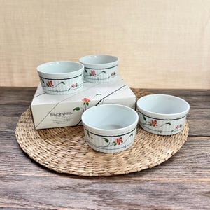 May include: A set of three white ceramic ramekins with vertical ribbing and a delicate floral pattern featuring pink flowers and green vines. The ramekins are displayed with their original white box labeled Savoir Vivre Spring Fancy.