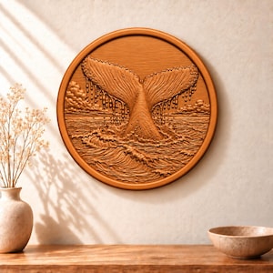 May include: A circular wooden wall plaque featuring a relief carving of a whale tail emerging from ocean waves. The design includes detailed water droplets falling from the tail, textured sea swells, and clouds on the horizon in a warm brown tone.