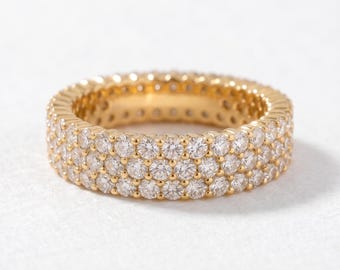 May include: A gold band ring featuring three parallel rows of small, round, clear, faceted stones set into the metal. The ring has a continuous design with stones covering the entire outer surface, creating a bright, reflective appearance.