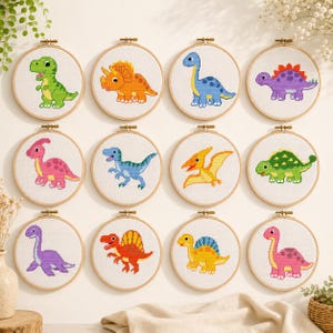Peut inclure: Douze tambours à broder circulaires en bois contenant des motifs de dinosaures au point de croix. Chaque tambour présente un motif de dinosaure unique et coloré sur tissu blanc, incluant des créatures vertes, orange, bleues, violettes, roses, jaunes et rouges.