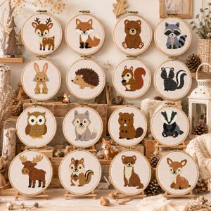 May include: A collection of sixteen circular wooden embroidery hoops, each featuring a cross-stitch design of a different woodland animal, including a deer, fox, bear, raccoon, rabbit, hedgehog, squirrel, skunk, owl, wolf, beaver, badger, moose, chipmunk, weasel, and fawn.