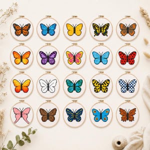 May include: A collection of twenty circular wooden embroidery hoops, each containing a unique pixel art butterfly design stitched onto white fabric. The butterflies feature diverse colour patterns, including solid, striped, spotted, and checkered motifs.