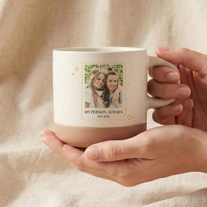 May include: A cream-colored ceramic mug with a speckled finish and a solid terracotta-colored base. The front features a rectangular photo of two people, with the printed text "MY PERSON, ALWAYS" and "EST 2026" below the image, accented by small gold stars.