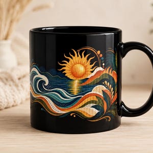 Könnte beinhalten: Ein schwarzer Keramikbecher mit einer lebendigen grafischen Illustration einer goldenen Sonne, die über stilisierten blauen Meereswellen und orangefarbenen Hügeln aufgeht. Das Design enthält fließende Linien und organische Formen in Gelb und Blau.