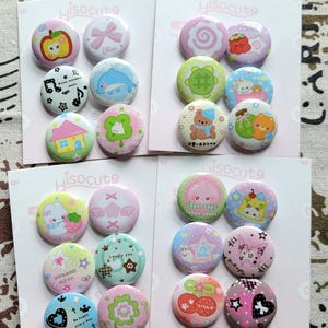 May include: A selection of Hisocute badges, each with a different design. The badges feature images of an apple, a bow, a dolphin, musical notes, a house, a four-leaf clover, a turtle, a bear, a bunny, stars, and cherries. The word "Hisocute" is printed on the cards.