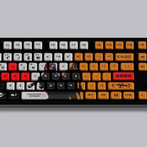 May include: Black mechanical keyboard with white, orange, and red keycaps. The keyboard features custom keycaps with text and graphics, including "CS:GO" and "Counter Strike".