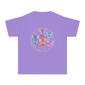 May include: A light purple t-shirt featuring a circular graphic print in the center. The design displays five diverse fairy characters with colorful wings, surrounded by small stars, crescent moons, and floral elements in shades of pink and blue.