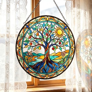 Può includere: Una vetrata rotonda raffigurante un albero con foglie colorate, frutta e un sole. L'opera presenta un fiume blu, montagne e un bordo floreale. È appesa a una catena davanti a una finestra con tende di pizzo.