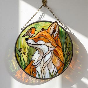 May include: A circular stained glass artwork depicting a fox with orange and white fur, a small bird, and green foliage. The piece is hung by a chain and hook. The fox is looking upwards with closed eyes, and the bird is perched on its head.