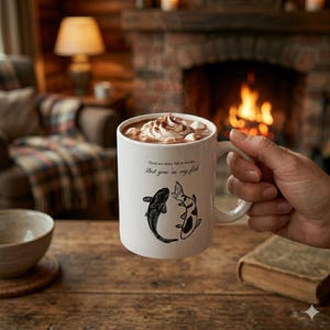 Puede incluir: Una taza de cerámica blanca llena de chocolate caliente, cubierta con crema batida y malvaviscos. La taza presenta dos ilustraciones de peces y el texto "There are many fish in the sea... But you're my fish."