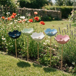 Peut inclure: Cinq abreuvoirs à oiseaux en céramique en forme de fleur sur de fins piquets en bois, disposés en rangée. Les bols sont bleu foncé, vert clair, blanc, bleu clair et rose clair. Chaque bol contient de l'eau et attire des abeilles.