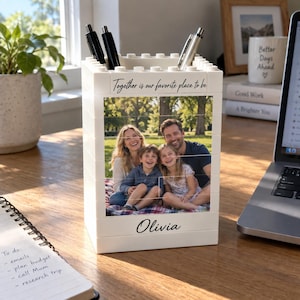Könnte beinhalten: Ein weißer, rechteckiger Schreibtisch-Organizer aus ineinandergreifenden Bausteinen. Die Vorderseite zeigt ein aufgedrucktes Foto einer vierköpfigen Familie sowie den Text "Together is our favorite place to be" und den Namen "Olivia".