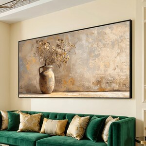 Può includere: Una grande opera d'arte su tela incorniciata raffigura una natura morta con un vaso rustico che contiene fiori secchi. L'opera presenta una tavolozza di colori neutri con toni beige, grigio e oro. Il dipinto è appeso sopra un divano di velluto verde con cuscini decorativi.