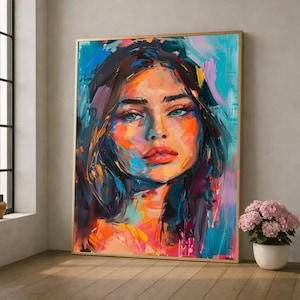 May include: A framed portrait painting of a woman with blue eyes and red lips. The artwork features bold brushstrokes in shades of blue, orange, and purple. The frame is gold, and the painting is displayed indoors.