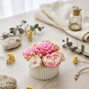 Peut inclure: Un récipient rond blanc cannelé rempli d'un arrangement décoratif de pièces de cire en forme de fleurs roses et blanches, agrémenté de petites fleurs séchées jaunes. L'arrangement présente des textures détaillées de pétales de rose et de marguerite.