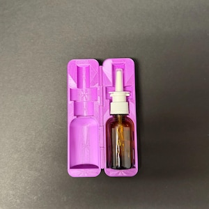 May include: A purple 3D-printed case, open to reveal a brown glass bottle with a white and clear nasal spray applicator. The case is designed to hold the bottle securely. The background is a solid dark gray.