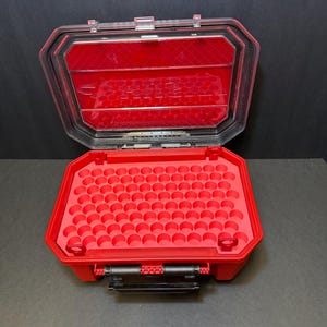 Pode incluir: Maleta de armazenamento de plástico vermelha aberta com tampa transparente. O interior apresenta uma inserção de espuma vermelha com inúmeros recortes circulares. A maleta está aberta, revelando o interior. Possui uma alça e dobradiças pretas.