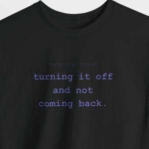 May include: A black short-sleeved t-shirt featuring the text "have you tried turning it off and not coming back." printed in a light purple, typewriter-style font centred on the chest area of the garment.
