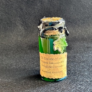 May include: A small glass bottle containing green liquid, sealed with a cork and black wax. The label reads "ID No: MW-CC-003, Name: Greenwake Mist, Origin: Greenwake, Mosswood Archives." A decorative leaf is attached.