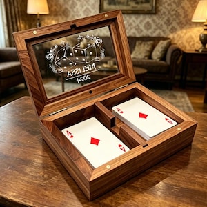 Könnte beinhalten: Eine Spielkartenbox aus Holz mit Glasdeckel, verziert mit einem Würfel- und Stern-Design. Die Box ist geöffnet und zeigt zwei Fächer mit Spielkarten. Der Text "MELISSA ASOS" ist auf das Glas geätzt.