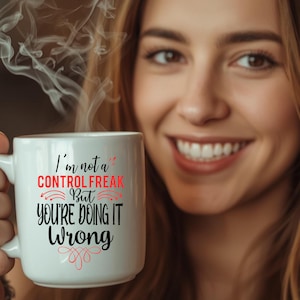 Pode incluir: Uma caneca de cerâmica branca com texto em preto e vermelho que diz: I'm not a CONTROL FREAK But YOU'RE DOING IT Wrong. A caneca tem uma alça no lado esquerdo e emite volutas de vapor pelo topo, indicando uma bebida quente no interior.
