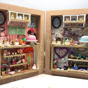 Puede incluir: Dos cajas de sombra enmarcadas con escenas de fiesta de té en miniatura. Cada caja presenta estantes llenos de tazas de té, teteras, pasteles y elementos decorativos. Una caja tiene un letrero que dice "Tea Times" y "Spring". Los marcos son de color marrón claro.