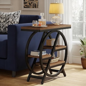 Puede incluir: Una mesa auxiliar con una encimera marrón oscuro y tres estantes. La mesa tiene una estructura de metal negro con un diseño en forma de rueda en los laterales. Una lámpara, libros y objetos decorativos están sobre la mesa.