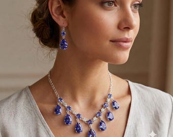 May include: A silver-toned necklace and matching drop earring set featuring multiple pear-shaped, deep blue faceted stones. The necklace consists of a delicate chain with dangling blue teardrop pendants, while each earring features a single matching blue teardrop stone suspended from a small circular stud.