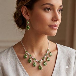 May include: A jewelry set consisting of a necklace and a pair of drop earrings. The necklace features a silver-toned chain with multiple pear-shaped, faceted green stones suspended in a symmetrical arrangement. Matching pear-shaped green stone earrings.