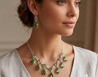 May include: A jewelry set consisting of a necklace and a pair of drop earrings. The necklace features a silver-toned chain with multiple pear-shaped, faceted green stones suspended in a symmetrical arrangement. Matching pear-shaped green stone earrings.