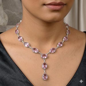 May include: A silver necklace featuring a series of oval-shaped, faceted light pink gemstones set in polished metal bezels. The design includes a central Y-shaped drop section with two additional oval pink stones hanging vertically from the center.
