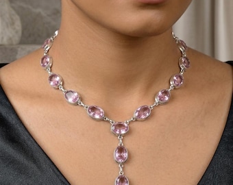May include: A silver necklace featuring a series of oval-shaped, faceted light pink gemstones set in polished metal bezels. The design includes a central Y-shaped drop section with two additional oval pink stones hanging vertically from the center.