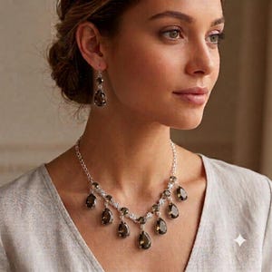 May include: A silver-toned necklace and matching drop earring set featuring faceted, pear-shaped smoky quartz stones. The necklace consists of a delicate chain with multiple dangling teardrop pendants, while each earring displays a single matching stone.