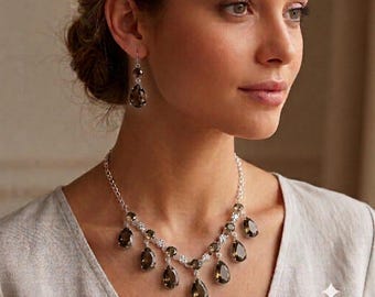 May include: A silver-toned necklace and matching drop earring set featuring faceted, pear-shaped smoky quartz stones. The necklace consists of a delicate chain with multiple dangling teardrop pendants, while each earring displays a single matching stone.