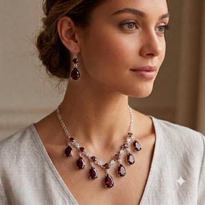 Può includere: Un set composto da una collana e orecchini pendenti in argento con pietre preziose rosso scuro sfaccettate a forma di pera. La collana presenta una sottile catena d'argento decorata con diverse pietre rosse a goccia pendenti e piccoli accenti.