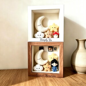 May include: Two shadow boxes, one white and one brown, each containing felted celestial figures. The white box has a crescent moon, stars, a cloud, and a mushroom. The brown box has similar figures, plus a doll. Text reads "Simply Us" and "Forever Memories".
