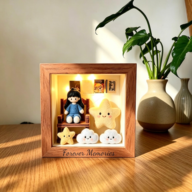 May include: A wooden shadow box with a miniature scene. Inside, a doll sits on a chair, surrounded by felt stars and clouds. The box is lit with small lights, and the words "Forever Memories" are inscribed on the frame.
