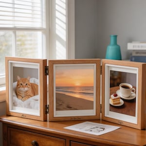 May include: A light wood triptych photo frame with three hinged panels. The left frame features an orange cat, the center frame shows a sunset beach, and the right frame displays a cup of coffee and cake. Each frame has a white mat and engraved text.