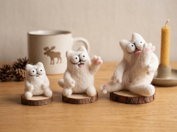A needle-felted 'derpy' cat portrait on a wood slice — genuinely one-of-a-kind slow craft that looks like a hilarious tiny oil painting brought to life in 3D fiber.