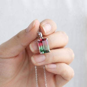 May include: A rectangular, emerald-cut pendant featuring a gradient of vibrant red transitioning into deep green, set in a polished silver-toned metal prong setting. The pendant hangs from a delicate, thin silver-toned chain necklace.
