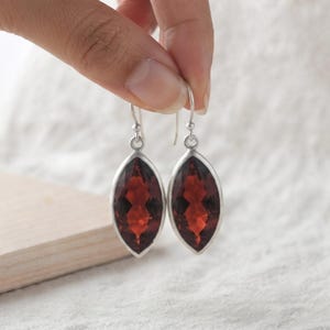 Peut inclure: Une paire de boucles d'oreilles pendantes avec des pierres précieuses facettées rouge foncé de taille marquise, serties dans des montures en argent poli. Les boucles d'oreilles sont suspendues à des crochets en argent simples et symétriques.