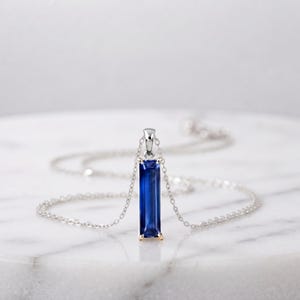 Può includere: Una collana color argento con un ciondolo verticale rettangolare in zaffiro blu profondo taglio baguette, tenuto da una montatura a quattro griffe. Il ciondolo è sospeso a una sottile e delicata catenina color argento.