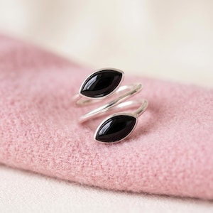 Könnte beinhalten: Ein offener Ring aus poliertem Silber mit zwei marquise-geschliffenen schwarzen Onyxsteinen an den Enden. Das Band ist spiralförmig gewunden und hebt die glatten, dunklen und reflektierenden Oberflächen der Steine vor dem silbernen Metall hervor.