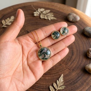 Elegant Moss Agate jewelry set displayed inside a luxury wooden jewelry box with soft pink velvet lining. The set includes a matching round Moss Agate pendant necklace and coordinating stud earrings, each featuring natural green moss-like inclusions within translucent white gemstones. The stones are bezel-set in gold-plated frames, creating a timeless and sophisticated look. This nature-inspired handmade jewelry set is perfect for weddings, bridesmaids, special occasions, and everyday wear,