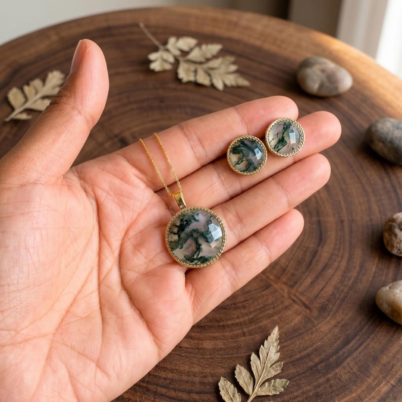 Elegant Moss Agate jewelry set displayed inside a luxury wooden jewelry box with soft pink velvet lining. The set includes a matching round Moss Agate pendant necklace and coordinating stud earrings, each featuring natural green moss-like inclusions within translucent white gemstones. The stones are bezel-set in gold-plated frames, creating a timeless and sophisticated look. This nature-inspired handmade jewelry set is perfect for weddings, bridesmaids, special occasions, and everyday wear,