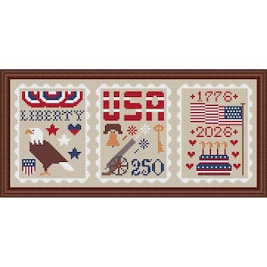 May include: Cross-stitch artwork featuring three postage stamp designs with patriotic themes. The stamps display the words "LIBERTY" and "USA", an eagle, a flag, and the years 1776 and 2026. The artwork is framed in a brown wooden frame.