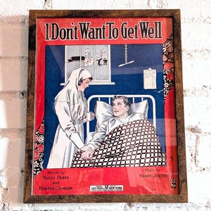 以下が含まれることがあります： 「I Don't Want To Get Well」というタイトルのヴィンテージな楽譜の表紙が額装されています。表紙には、白い制服を着た看護師と、病院のベッドに横たわる男性が描かれています。楽譜は赤い紙に黒の文字で印刷されており、背景は青色です。