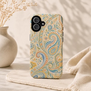 Op de afbeelding: Een telefoonhoesje met een kleurrijk paisley patroon in blauw, geel, oranje en groen. De hoes heeft een zwarte cameramodule en zijknoppen. Het ontwerp doet denken aan vintage textiel.