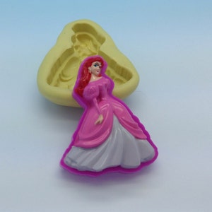 May include: A silicone mold for making a cake topper or figurine of a princess in a pink and white dress. The mold is yellow and the princess is pink and white.